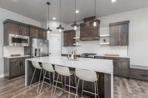 Kitchen with dark wood finish cabinetry, tasteful backsplash, light stone countertops, pendant lighting, and stainless steel appliances