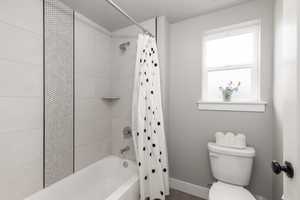 Bathroom featuring toilet and shower / bath combination with curtain