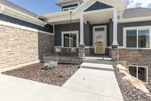 Property entrance featuring covered porch, stone siding, board and batten siding, and roof with shingles