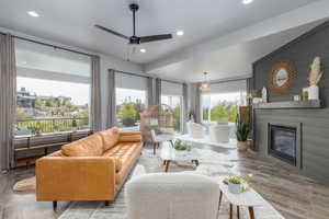 Living room with wood finished floors, a ceiling fan, a glass covered fireplace, and recessed lighting