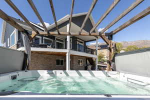 Back of house featuring brick siding, a mountain view, a hot tub, a patio area, and a balcony