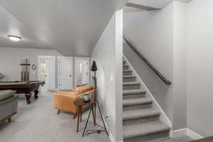 Stairs featuring carpet flooring, pool table, and a textured ceiling