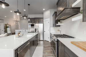 Kitchen with stainless steel appliances, dark wood finish cabinets, light stone counters, open shelves, and light wood-style floors