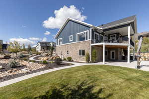 Rear view of house with board and batten siding, a yard, stone siding, a patio, and a balcony