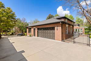 View of property exterior with concrete driveway, brick siding, a gate, a garage, and a chimney