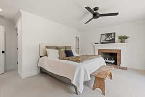 Bedroom featuring ornamental molding, light colored carpet, a ceiling fan, and a fireplace