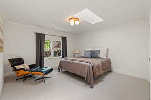 Bedroom featuring a skylight, light carpet, and ornamental molding