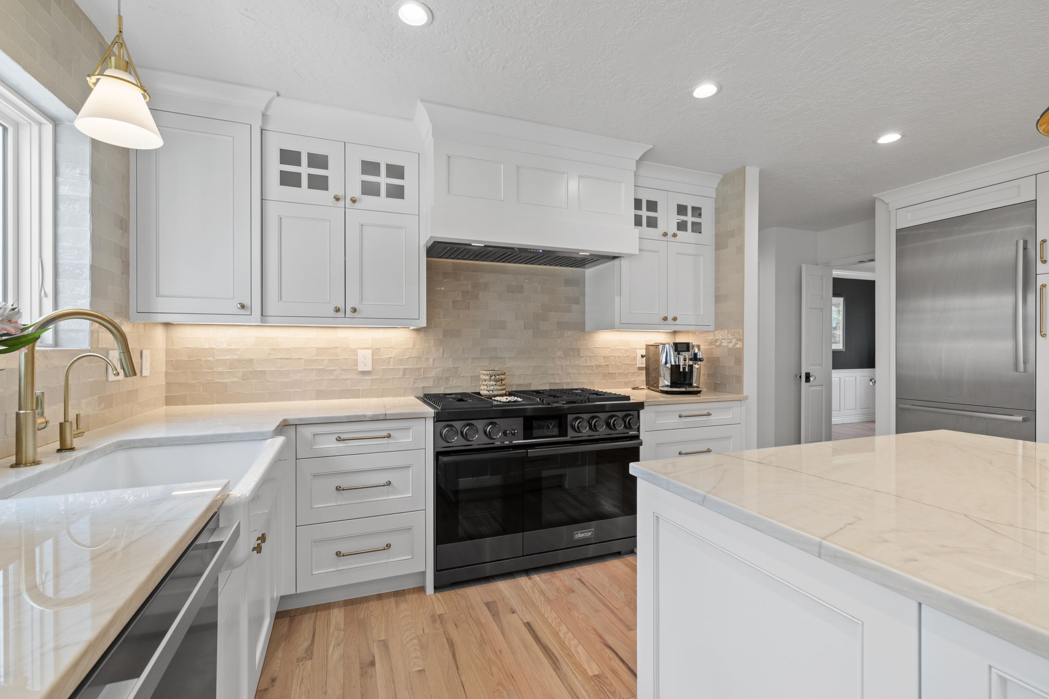 Kitchen with white cabinetry, premium appliances, glass fronted cabinets, and tasteful backsplash