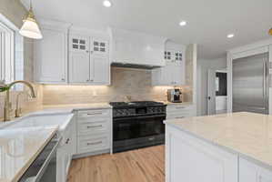 Kitchen with white cabinetry, premium appliances, glass fronted cabinets, and tasteful backsplash