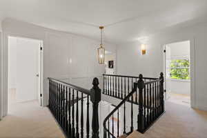 Corridor featuring an upstairs landing, light carpet, and ornamental molding