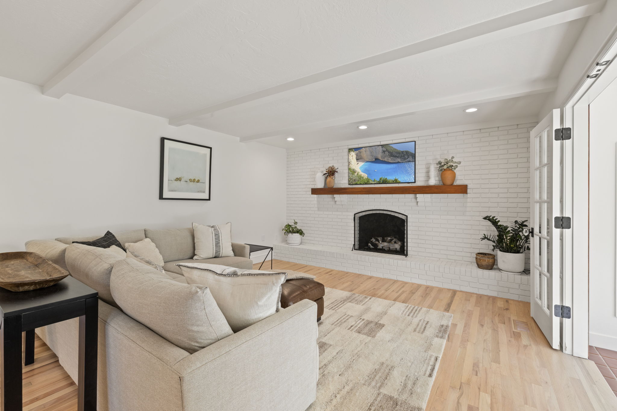 Living area with brick wall, a brick fireplace, beamed ceiling, light wood-style floors, and recessed lighting