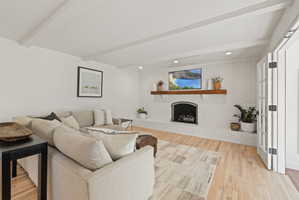 Living area with brick wall, a brick fireplace, beamed ceiling, light wood-style floors, and recessed lighting