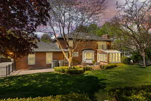 Back of house at dusk with brick siding, a sunroom, a patio area, and a chimney
