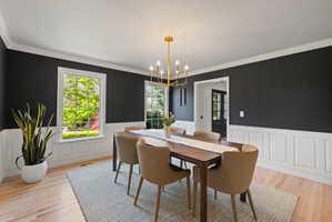 Dining room with a chandelier, wainscoting, light wood finished floors, crown molding, and a textured ceiling
