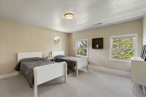 Bedroom with wallpapered walls, light colored carpet, and a textured ceiling