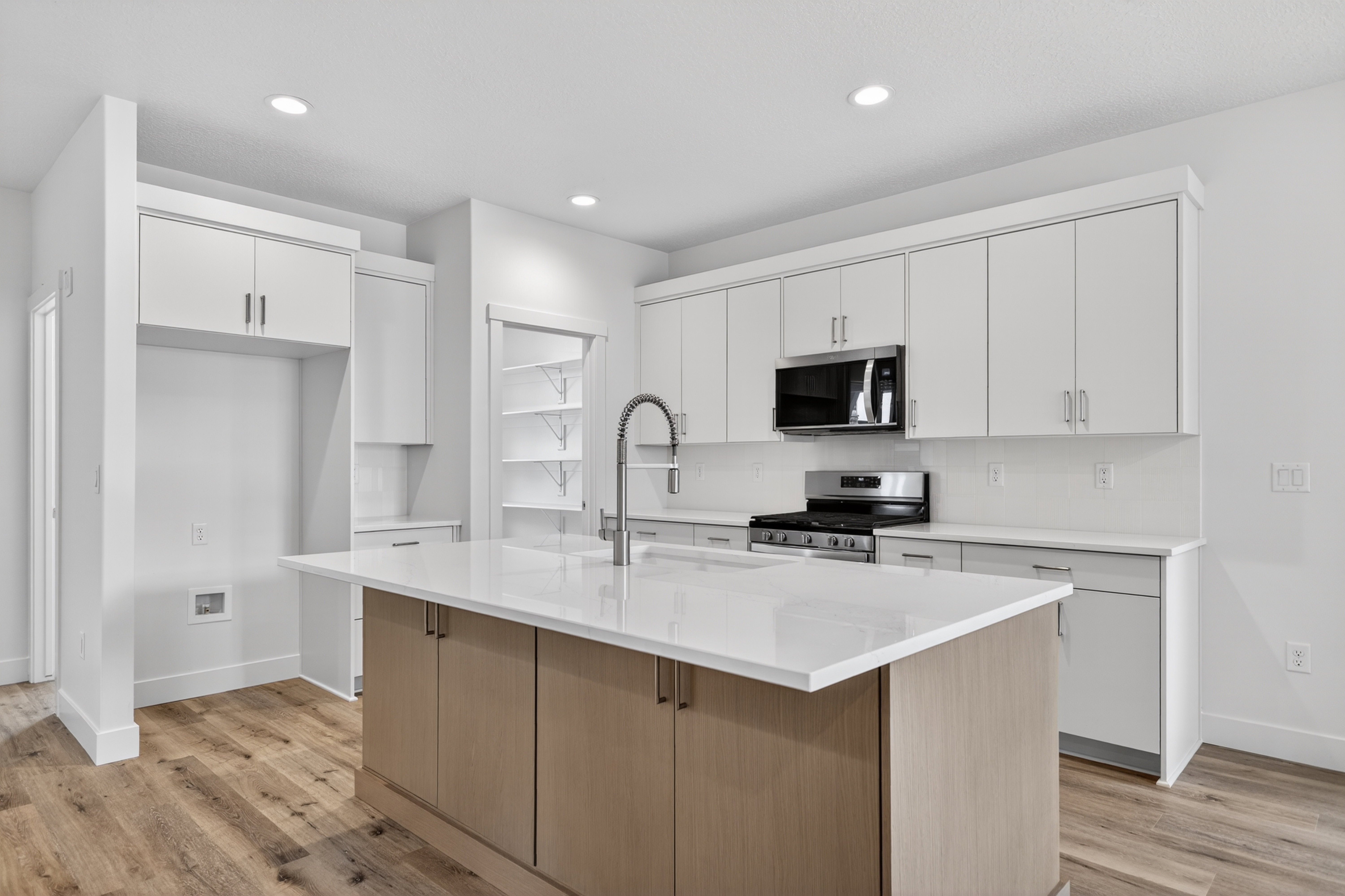 Dual tone kitchen featuring two tone cabinetry, stainless steel appliances, a center island with sink, light wood-style floors, and recessed lighting