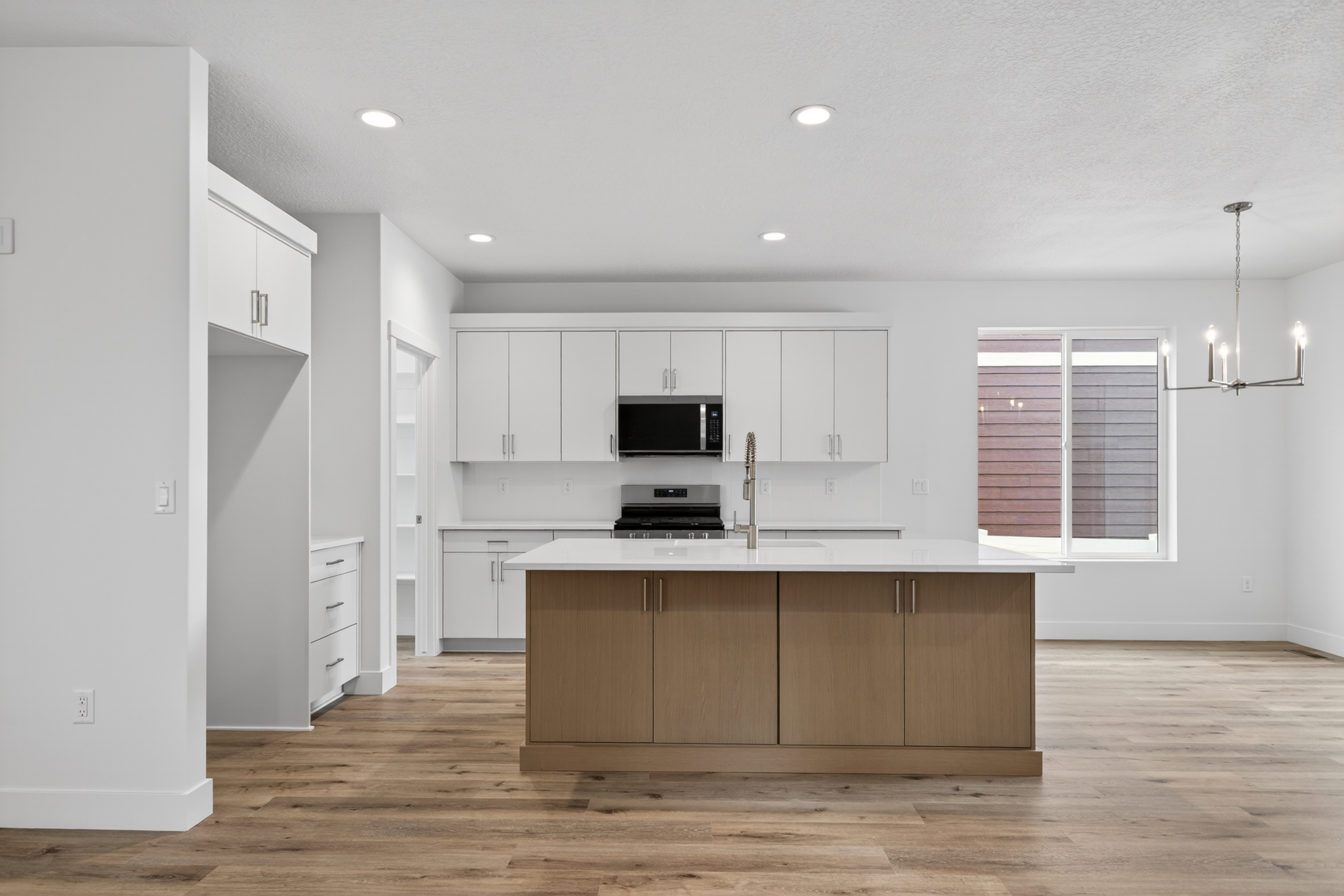 Kitchen featuring an island with sink, light wood-style floors, suspended lighting, stainless steel appliances, and two tone cabinets
