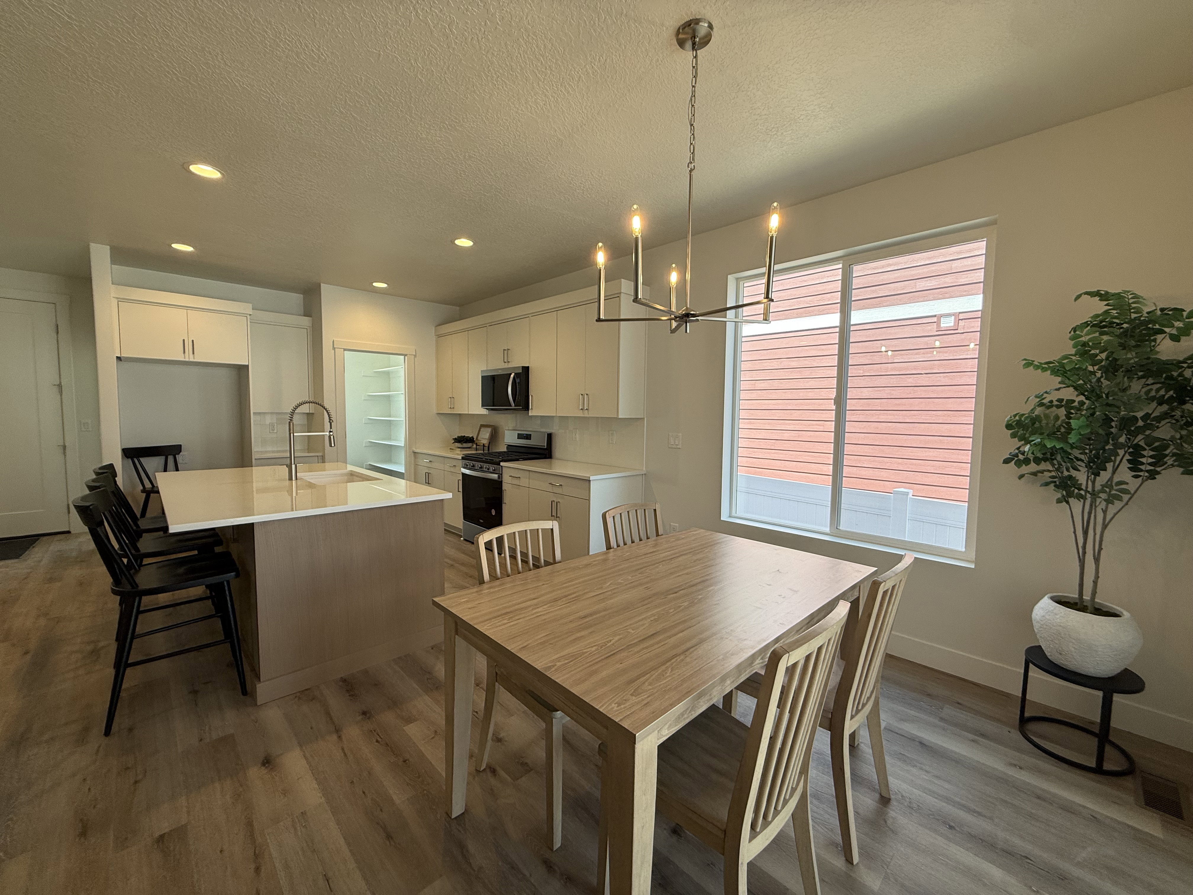 Open-concept kitchen and dining area featuring wood-finish flooring, a kitchen island with seating, pendant lighting, stainless steel appliances, and ample natural light from a large window
