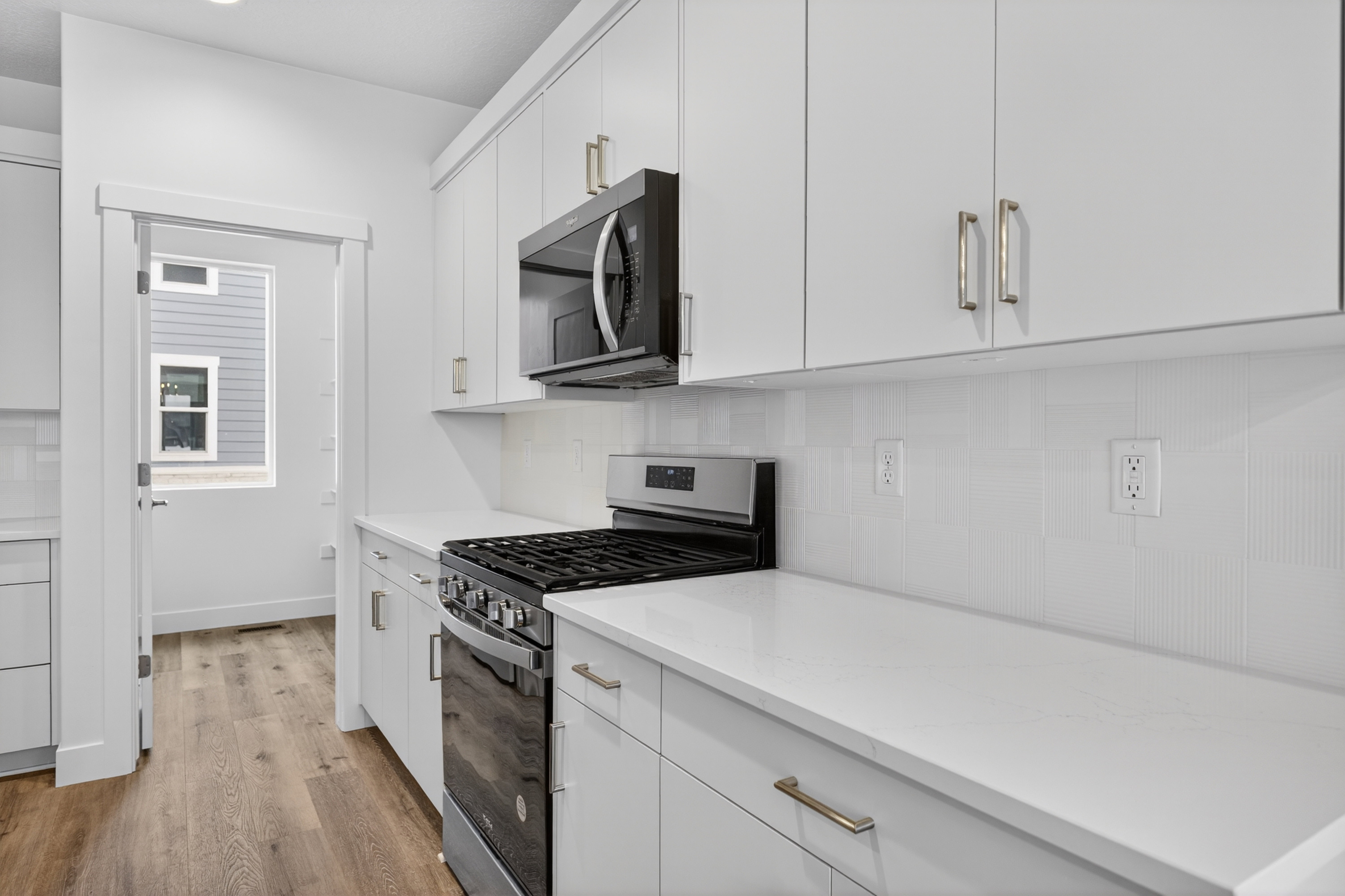 Kitchen with stainless steel appliances, white cabinetry, light wood-style floors, decorative backsplash, and light stone counters