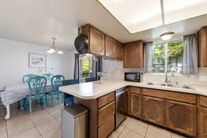 Kitchen featuring wood finish cabinetry, light countertops, a peninsula, light tile patterned flooring, and plenty of natural light