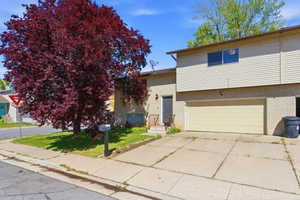 Tri-level home with concrete driveway, a front lawn, an attached garage, and brick siding