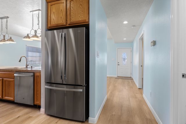 Kitchen with stainless steel appliances, wood finish cabinetry, light wood-type flooring, a textured ceiling, and recessed lighting