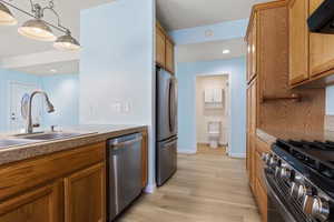 Kitchen featuring stainless steel appliances, light wood-type flooring, pendant lighting, extractor fan, and wood finish cabinets