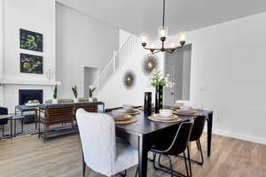 Dining room with light wood-type flooring, a chandelier, a glass covered fireplace, and a high ceiling