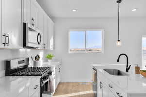 Kitchen featuring white cabinets, stainless steel appliances, light wood-style flooring, and light stone counters