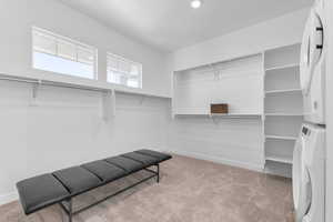 Walk in closet with light carpet and stacked washer / dryer