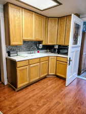 Kitchen featuring light countertops, light wood-type flooring, black microwave, decorative backsplash, and light wood finish cabinets