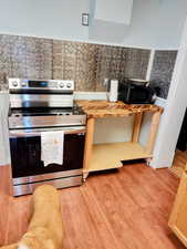 Kitchen with electric stove, light wood-type flooring, wooden counters, and tile walls