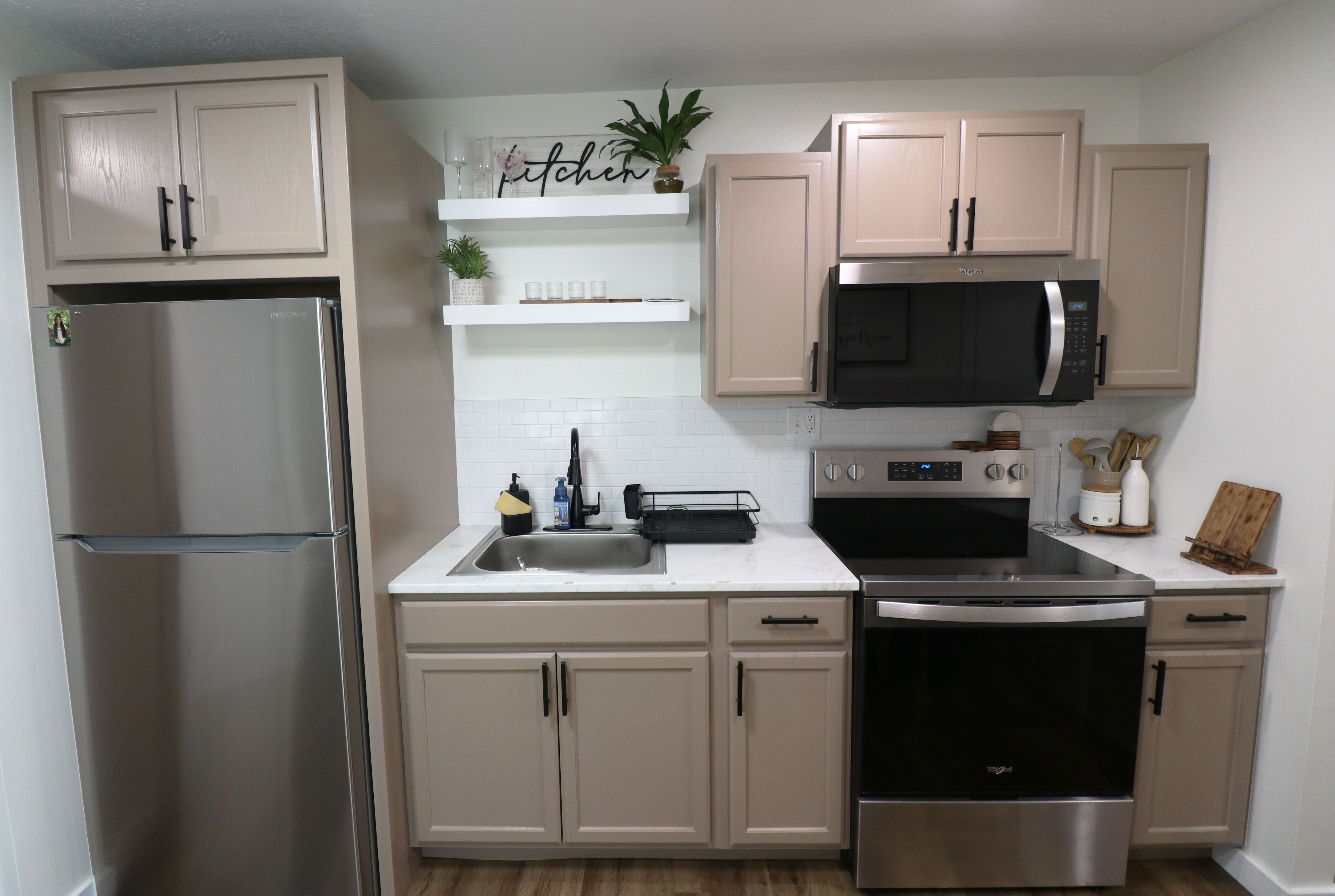 Kitchen with stainless steel appliances, open shelves, backsplash, dark wood-style flooring, and light stone countertops