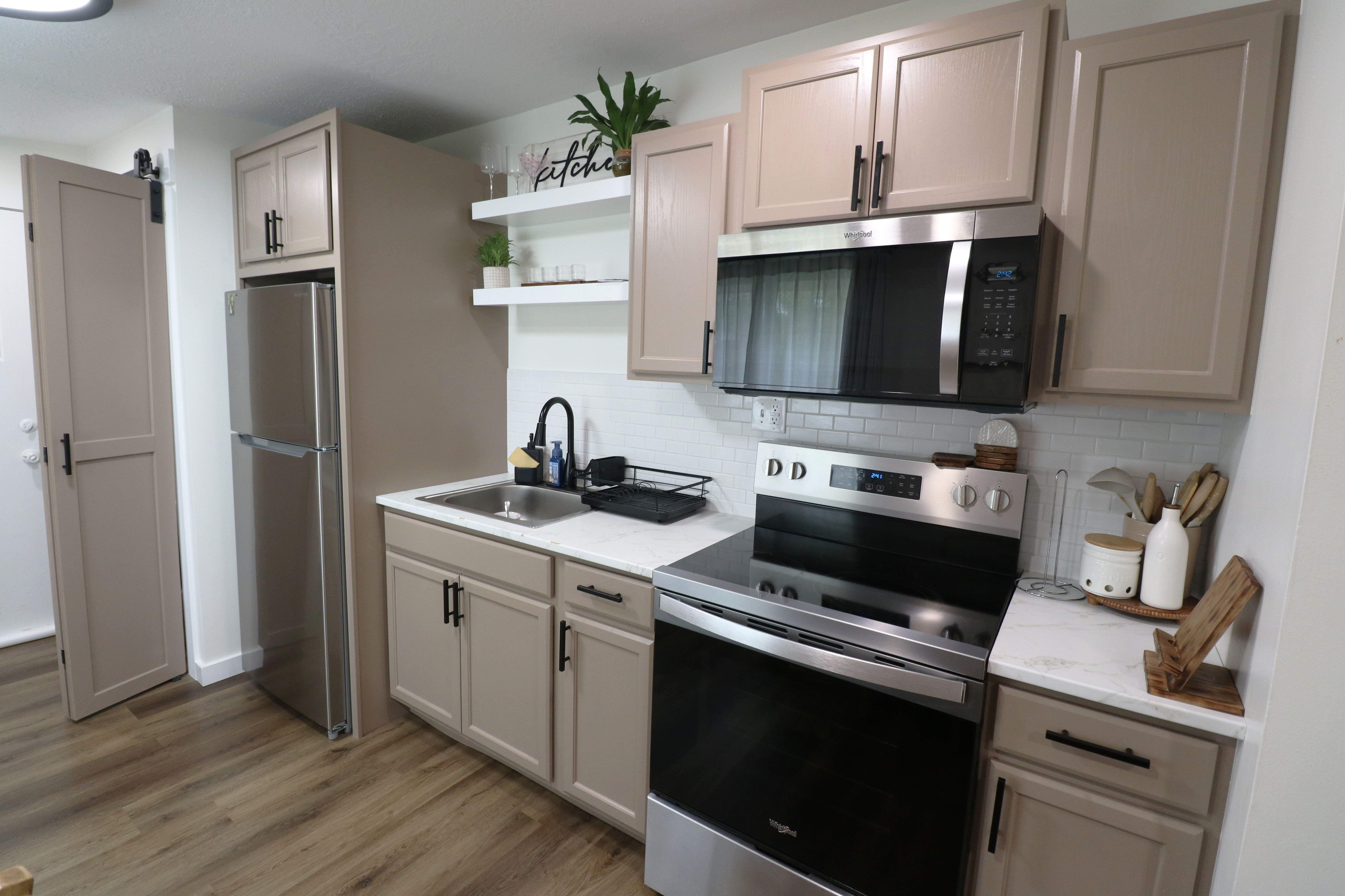 Kitchen with stainless steel appliances, open shelves, dark wood-style floors, decorative backsplash, and light stone counters