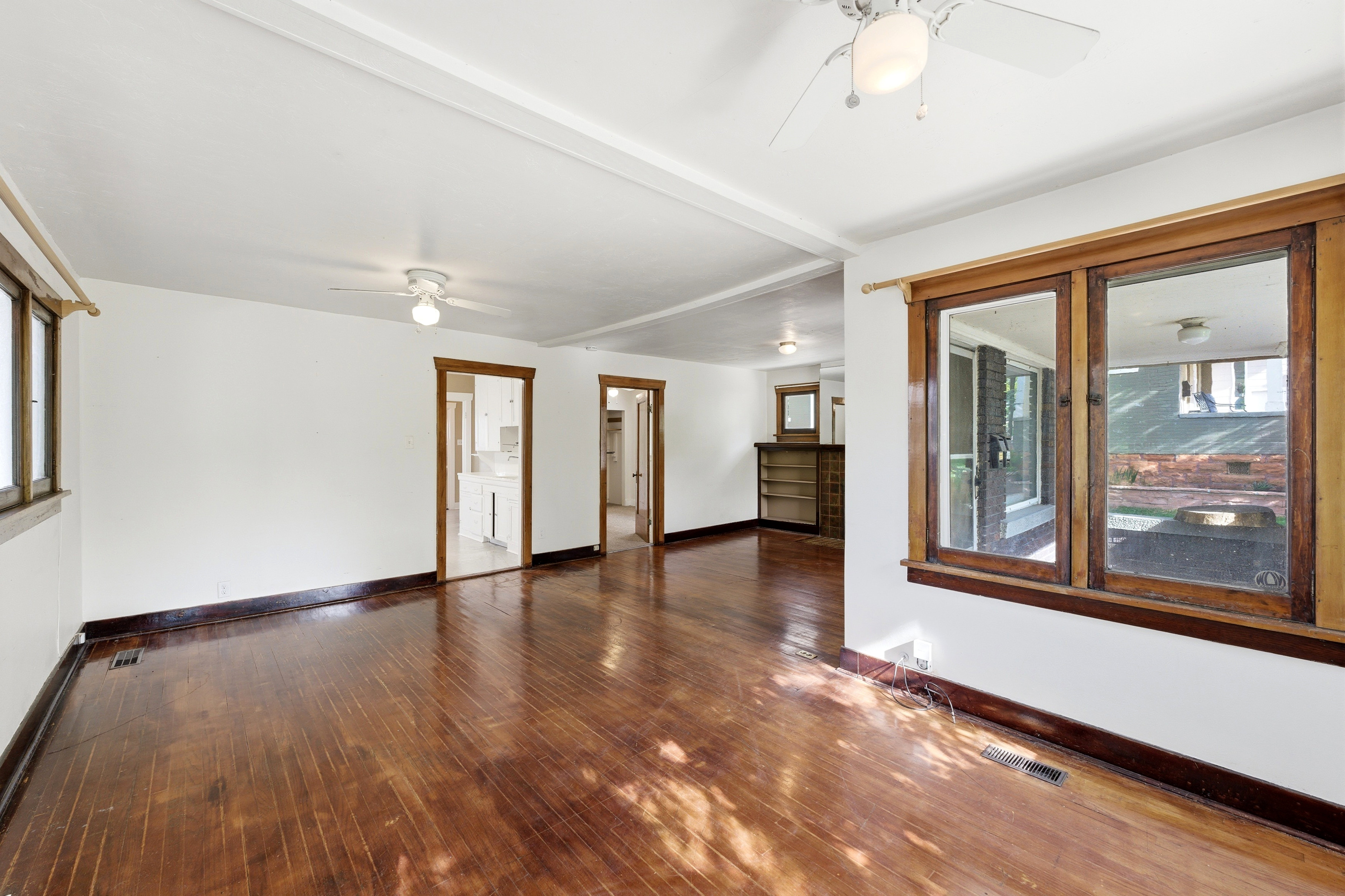 Unfurnished living room with a ceiling fan, dark wood-type flooring, and beam ceiling