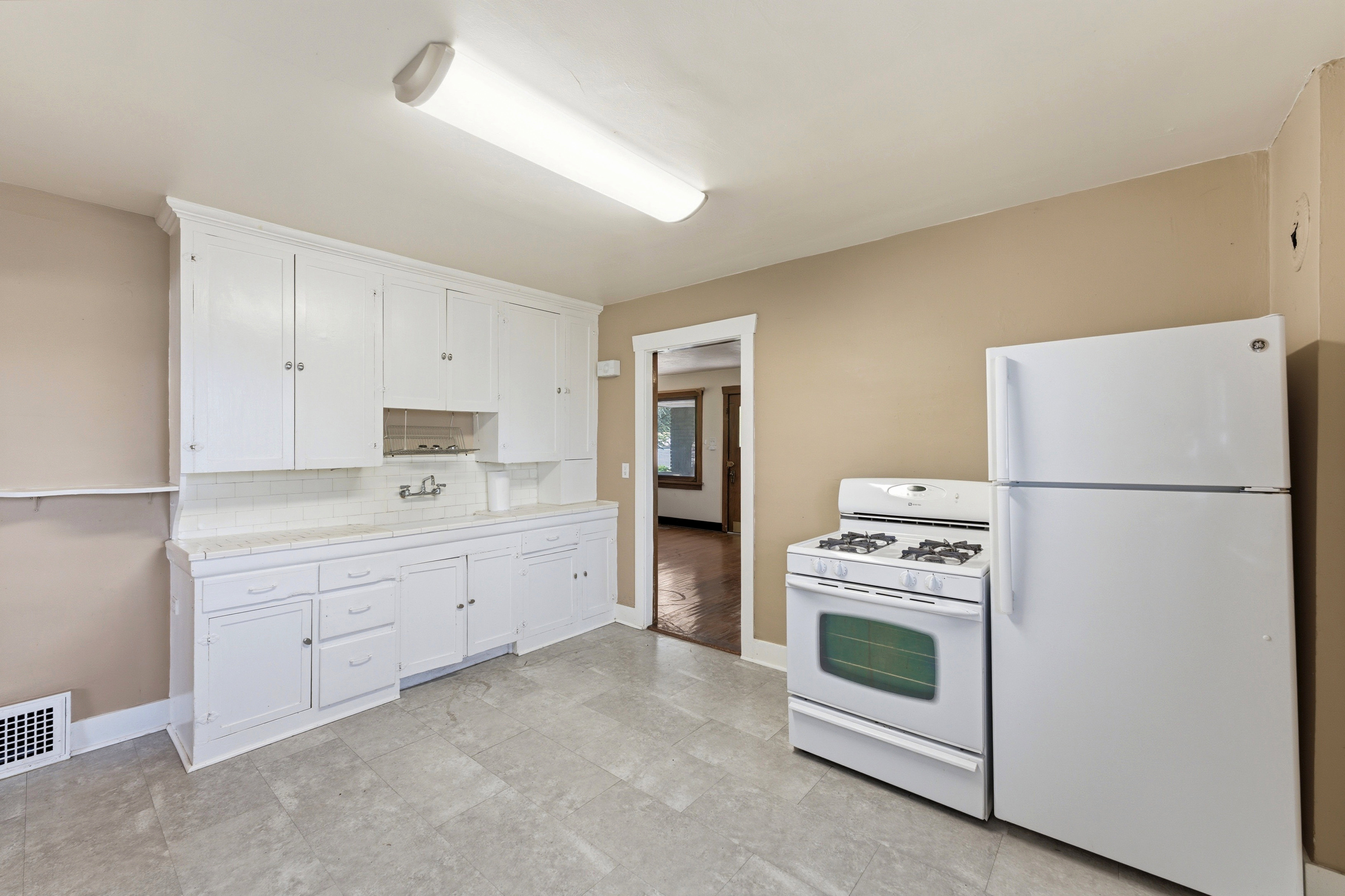 Kitchen with white appliances, white cabinetry, light countertops, and backsplash