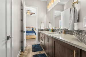 Ensuite bathroom featuring double vanity, light wood finished floors, and a ceiling fan
