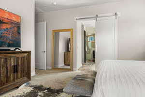 Bedroom featuring a barn door, light carpet, and ensuite bath