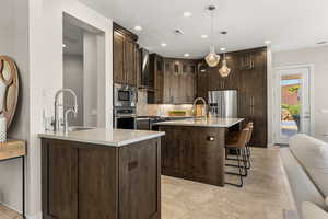 Kitchen featuring dark wood finish cabinetry, a kitchen bar, light stone counters, premium appliances, and decorative backsplash