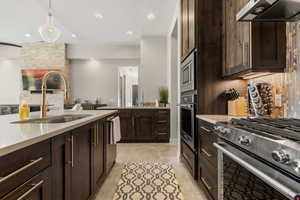 Kitchen featuring stainless steel appliances, dark wood finish cabinetry, pendant lighting, and light stone counters