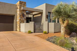 View of side of home featuring a gate, a garage, stone siding, stucco siding, and concrete driveway