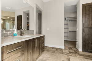 Full bath with a walk in closet, vanity, and tasteful backsplash
