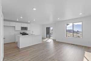 Kitchen with white cabinetry, light wood-type flooring, a center island with sink, stainless steel appliances, and recessed lighting