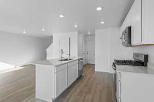 Kitchen with a kitchen island with sink, stainless steel appliances, white cabinets, dark wood finished floors, and recessed lighting