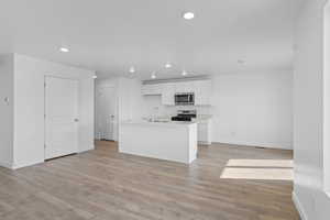 Kitchen with an island with sink, white cabinets, stainless steel appliances, light wood-style flooring, and recessed lighting