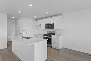 Kitchen featuring white cabinetry, stainless steel appliances, an island with sink, dark wood-style floors, and recessed lighting