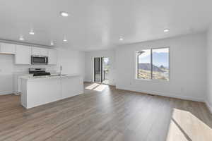 Kitchen with white cabinets, open floor plan, light wood-type flooring, a kitchen island with sink, and stainless steel appliances