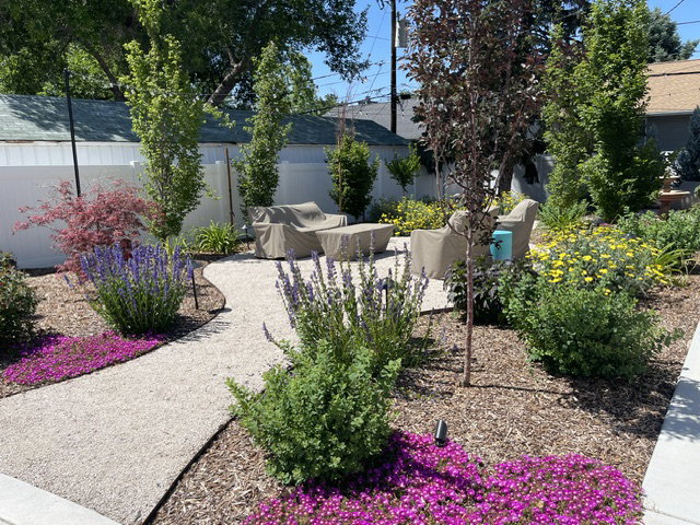 Gravel pathway leading to a dedicated outdoor patio area, surrounded by extensive landscaping with mature trees, flowering shrubs, and groundcover
