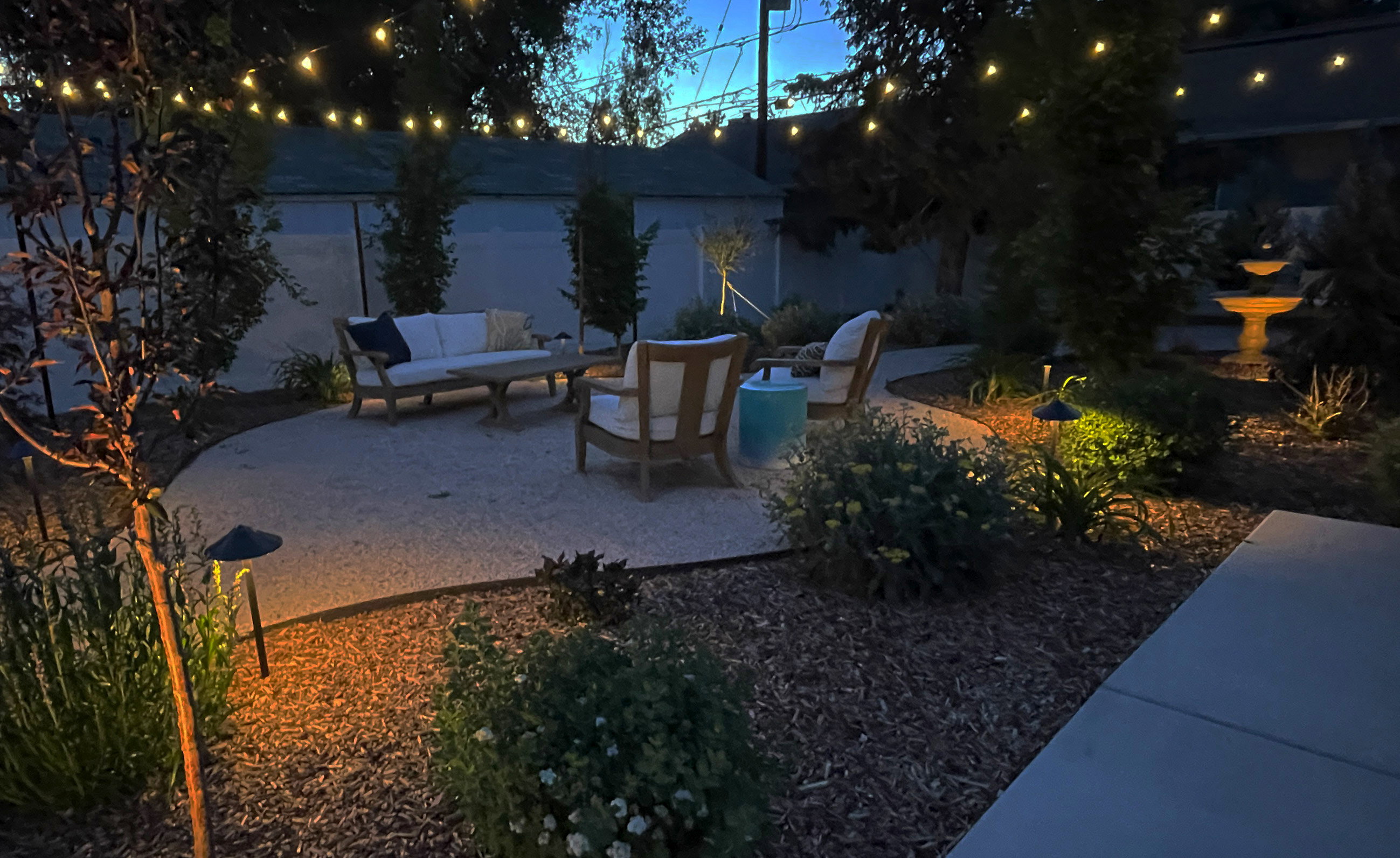 Landscaped exterior featuring a gravel patio, string lighting, and in-ground accent lighting