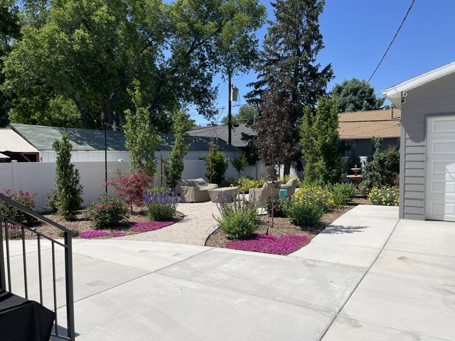 Landscaped rear yard featuring a pea gravel patio, mature trees, flowering shrubs, and a decorative water feature